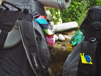 Zaini da trekking Quechua Forclaz 70 con borracce e oggetti colorati fissati all'esterno con spilla decorativa a forma di lumaca simbolo dello slow travel