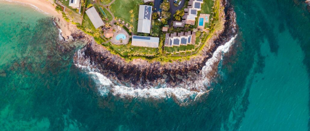 Veduta aerea dall’alto della costa di Lahaina a Maui (Hawaii), con promontorio di roccia lavica, resort con pannelli solari e piscine, acqua turchese e aree più scure di barriera corallina nel Pacifico.