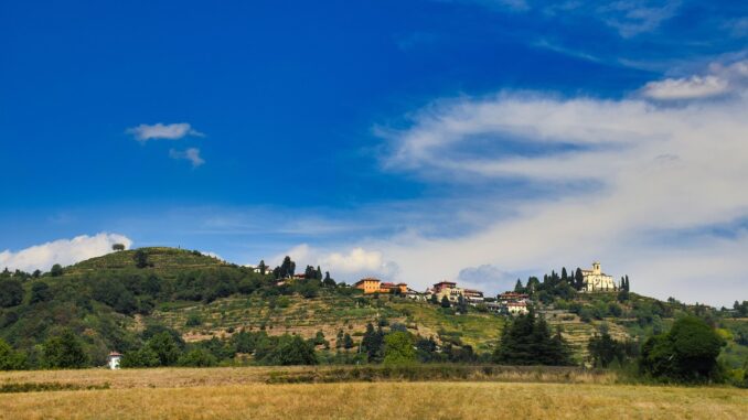 Campi e colline terrazzate di Montevecchia in Brianza, con case e una chiesa sul crinale sotto il cielo azzurro