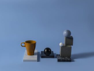 Tazza ocra e oggetti geometrici su sfondo azzurro.