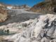 Ghiacciaio alpino parzialmente coperto da grandi teli bianchi, circondato da montagne rocciose