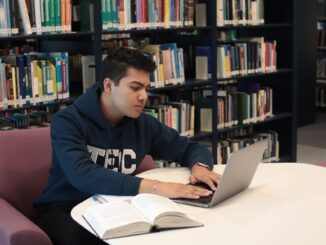 ersona seduta in biblioteca usa un computer portatile accanto a libri e quaderni