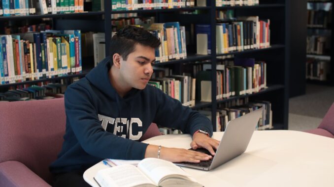 ersona seduta in biblioteca usa un computer portatile accanto a libri e quaderni