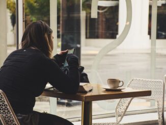 Donna usa lo smartphone mentre beve un caffè seduta a un tavolo