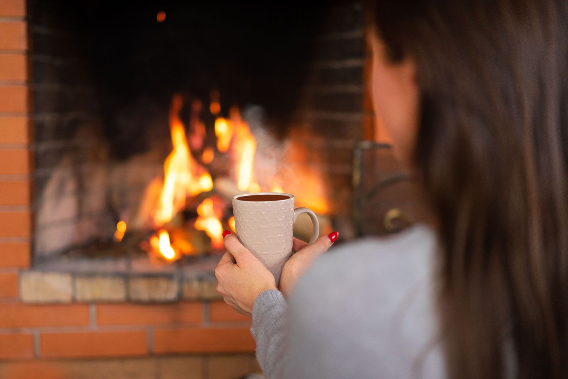 Donna con una tazza di bevanda calda davanti a un camino a legna acceso, in un ambiente domestico